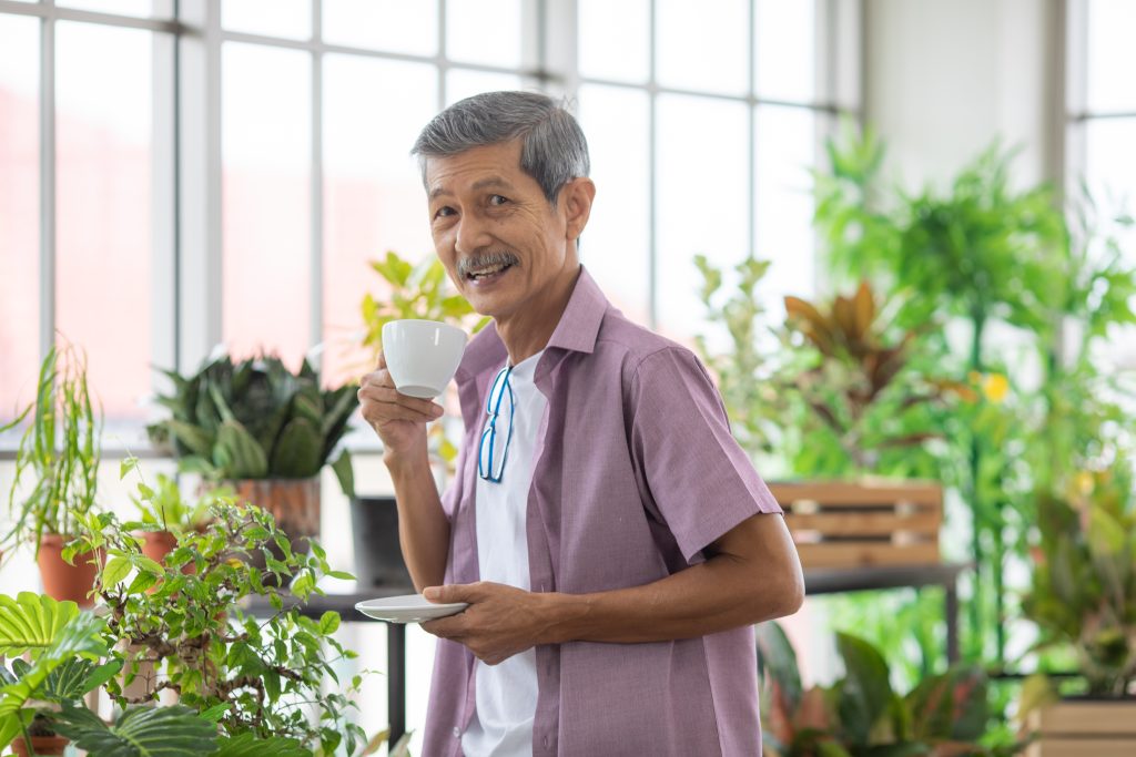 man standing among indoor plants enjoying a cup of tea