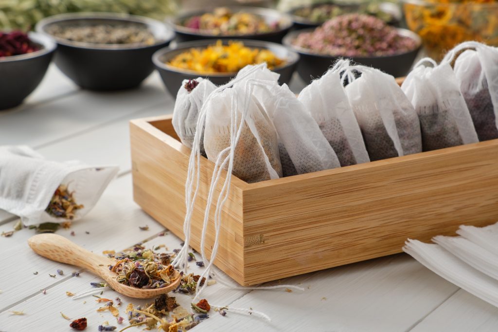 wooden tray with filled homemade teabags, bowls of fresh herbals in the background